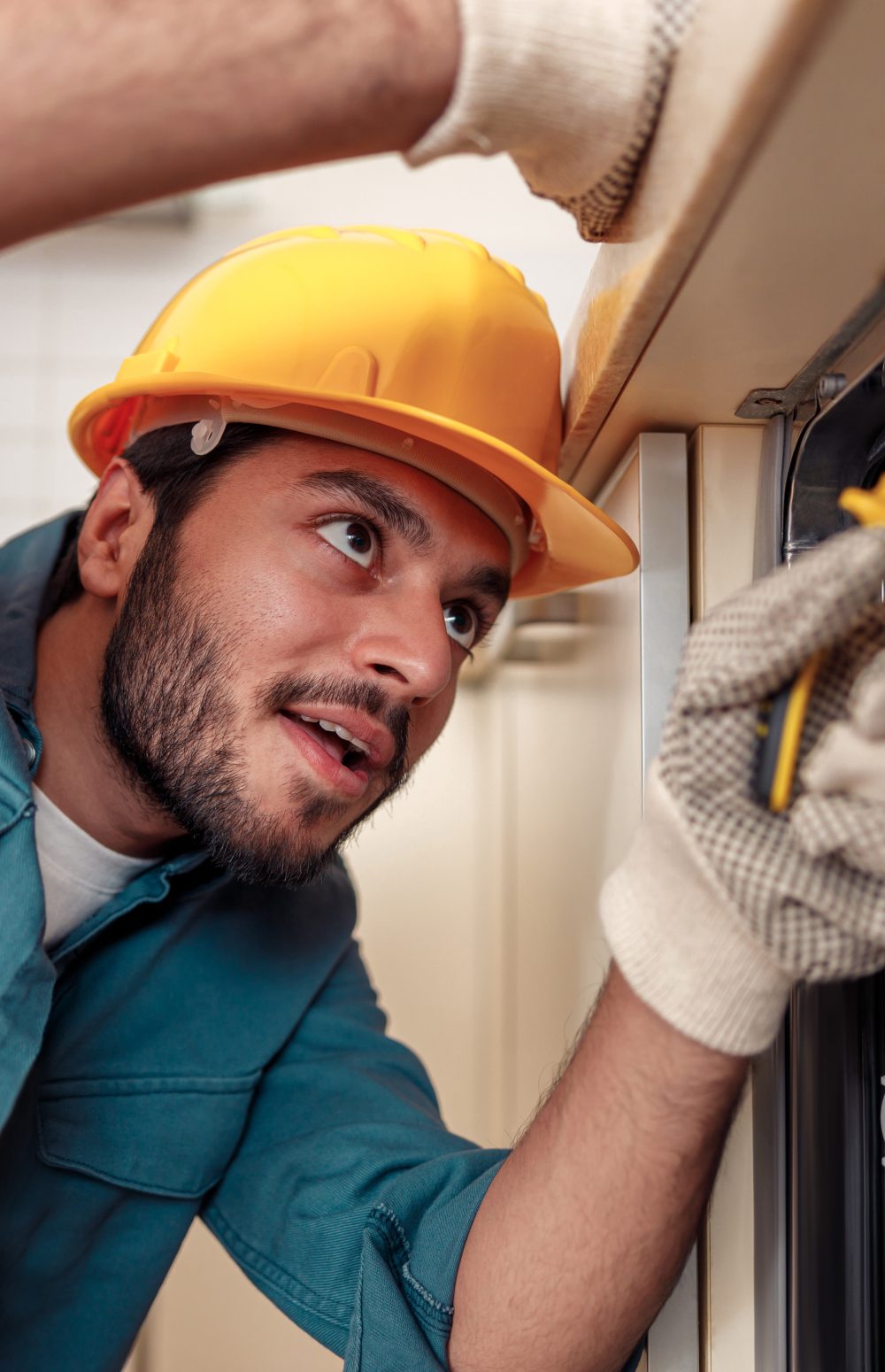 Close up of handyman in special clothing repairing dishwasher in modern kitchen